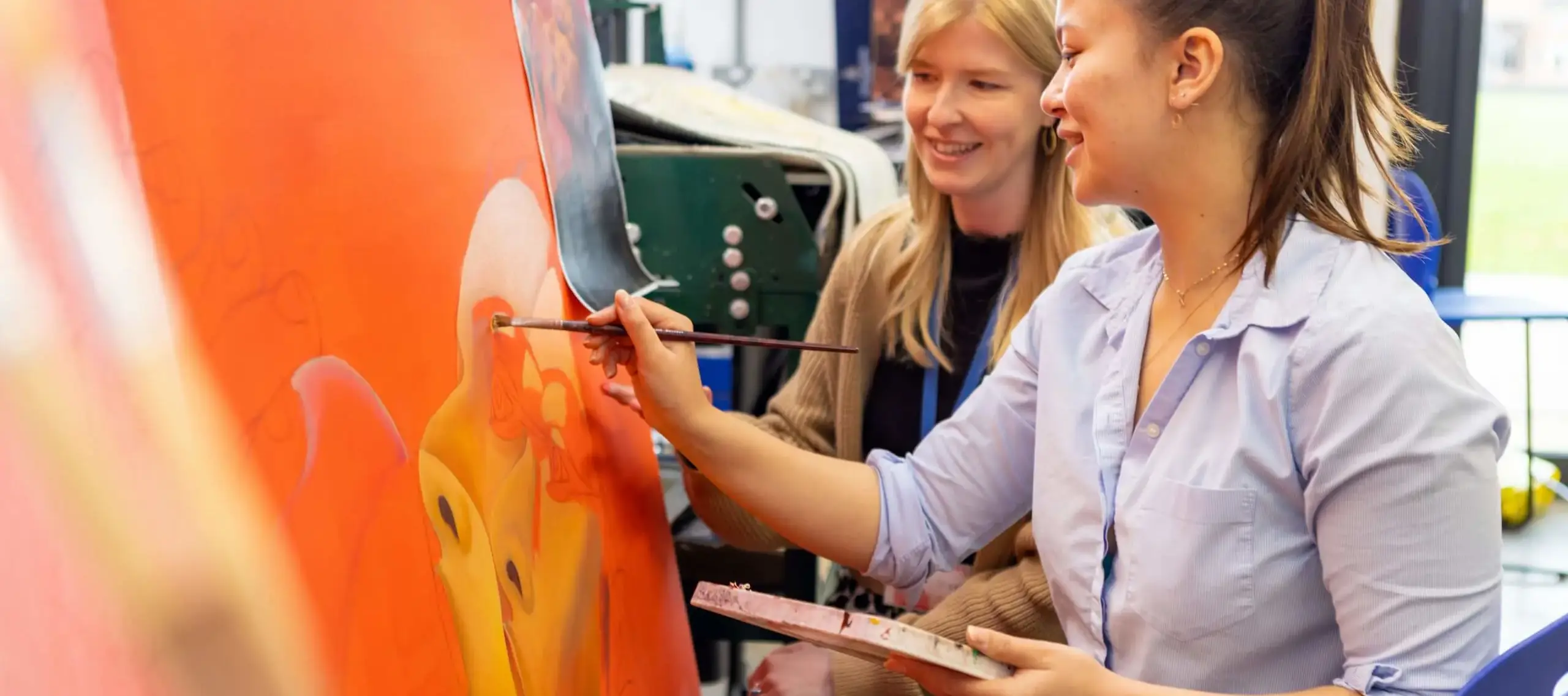 Sixth former and art teacher in art and design centre working on a large orange painting