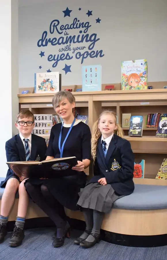 Pocklington Prep School headteacher sits with two pupils in the library reading together 