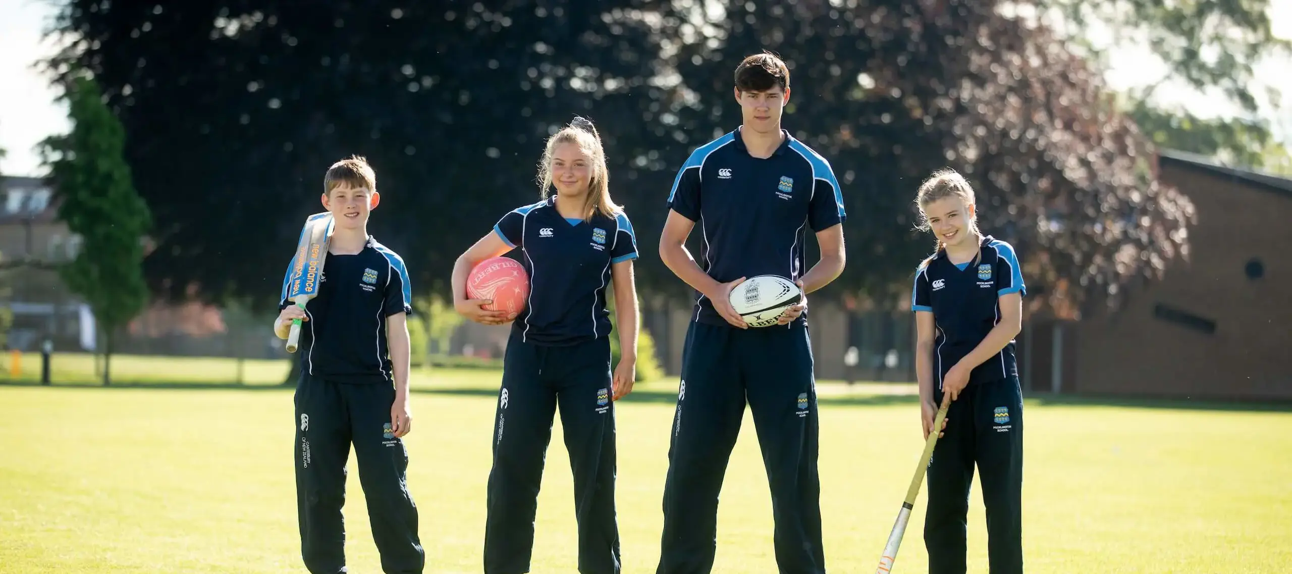 Four Pocklington School pupils in sports kit with sports props on a field