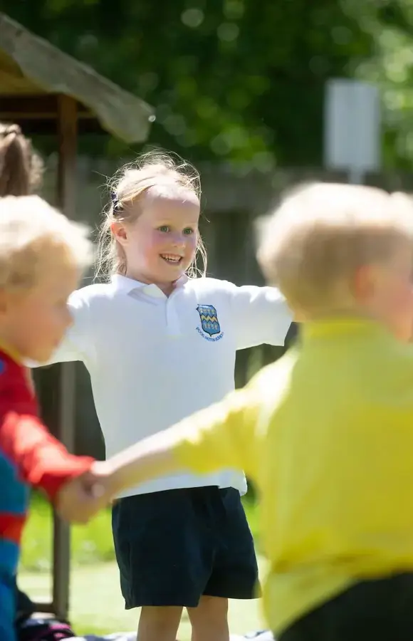 Pocklington early years pupils outside holding hands in a circle, smiling.