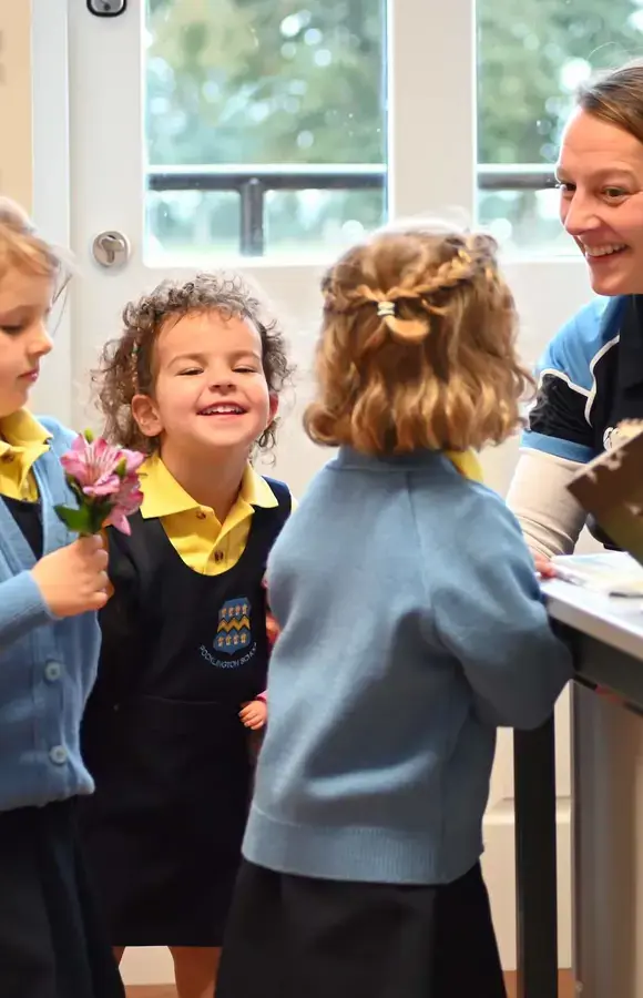 Pocklington Pre-School pupils holding a dolls and flowers with teacher smiling at each other